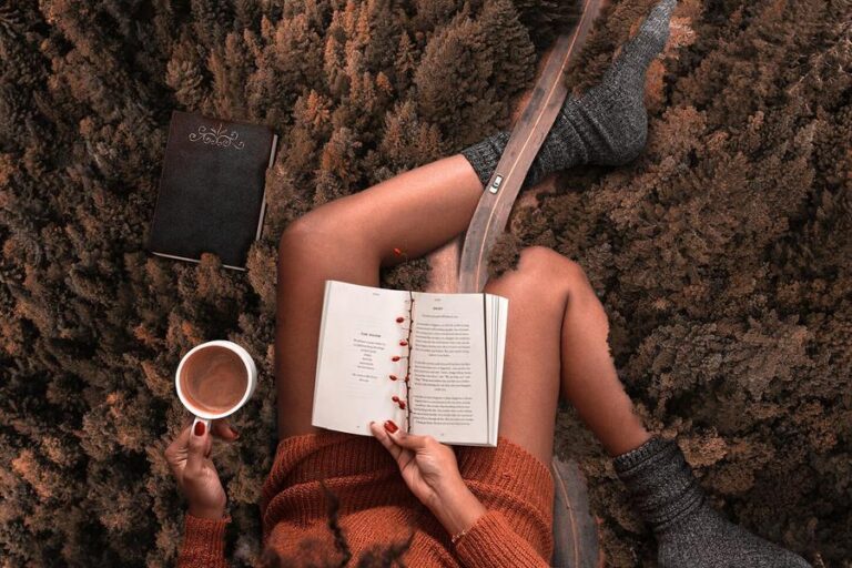 A collage composed by a road in the middle of a wood plenty of pines, going under gigantic women's legs. She's grabbing, at the time, a cup of coffee, while reading a paper book
