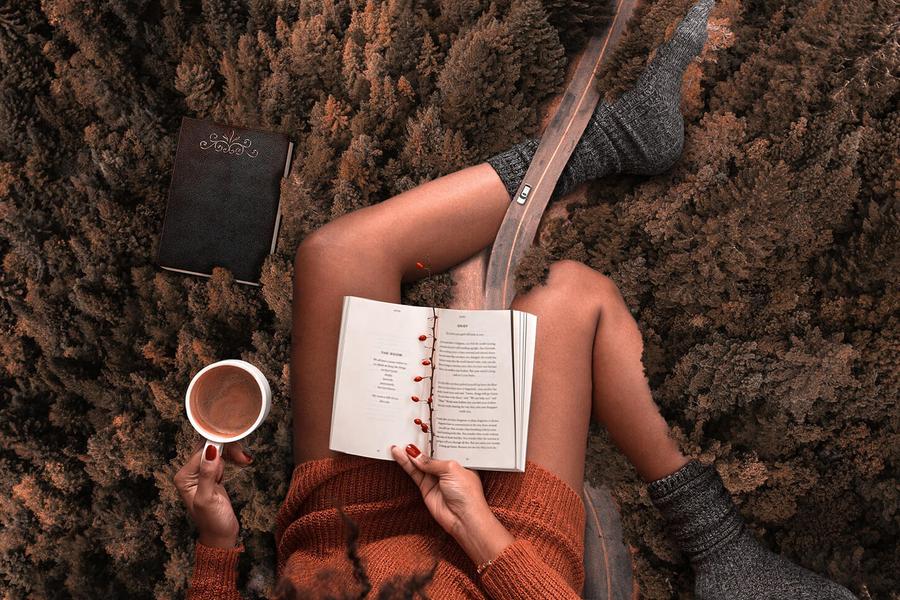 A collage composed by a road in the middle of a wood plenty of pines, going under gigantic women's legs. She's grabbing, at the time, a cup of coffee, while reading a paper book