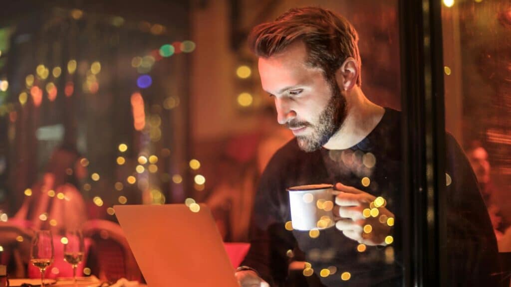 A man drinking his coffee while reading on his laptop, in a very illuminated bar