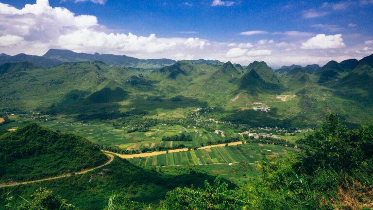 A green landscaping, with some mountains far away and a couple of white clouds on a blue sky